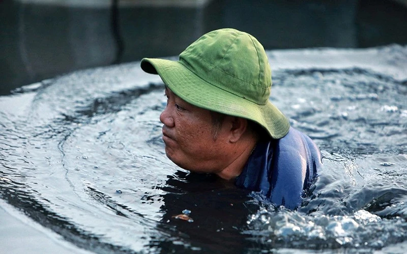 Một công nhân thoát nước dầm mình dưới dòng nước đen ngòm để sửa ống hút nước trên kênh Lò Gốm (TP Hồ Chí Minh). Ảnh: Ngọc Dương